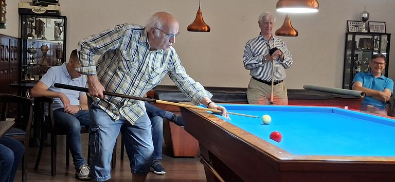 Spelers en toeschouwers rond het biljart tijdens de competitie